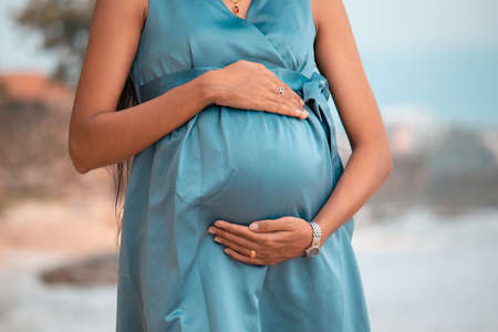 Pregnant Lady holds belly in both hands in beach background natural light conditions portraiture...