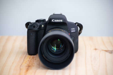 Galle, Sri Lanka - 02 18 2021: Canon EOS 800D also known as rebel t7i DSLR camera and the mounted Tokina 100mm 2.8 macro lens with lens cap front view, on a wooden table, neutral color background.のeditorial素材