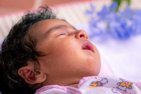 1-Month-old cute baby girl sleeping in a pink fluffy pillow, born with lots of black hair. Napping...