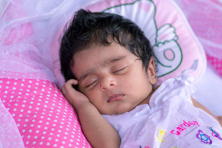 1-Month-old cute baby girl sleeping in a pink fluffy pillow, born with lots of black hair. Napping and dreaming time for the adorable healthy infant. close up photograph of small child portraiture.のeditorial素材