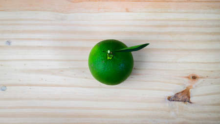 Isolated Citrus Sinensis fruit (Sweet orange) in the middle of the wooden cutting board overhead view. Copy space for text around the fresh raw fruit. Single leaf attached to the stem of the orange.の写真素材