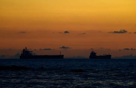 Empty cargo ships on the horizon, misty pastel sunset colors in the sky, and silhouetted ships. Scenic landscape photograph near the beach in Galle, Sri Lanka.の写真素材