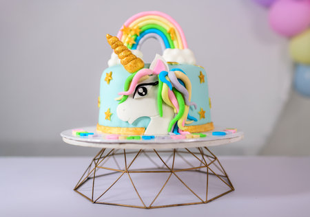 Beautiful unicorn-themed baby girls birthday cake on a stand. Cute unicorn face and the...