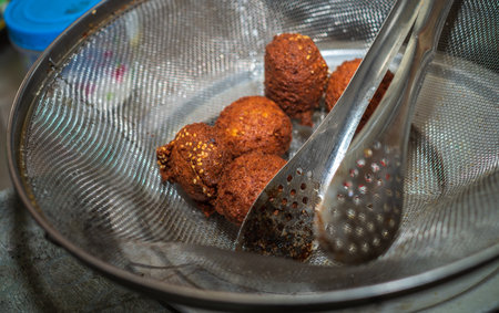 Straining excess oil from deep-fried golden browned falafels. stainless steel tongs and the strainer close up.の写真素材