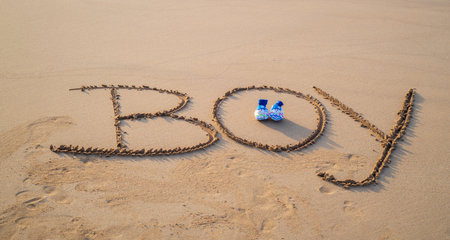 Writing of the word BOY on the sandy beach, baby shoes in the middle.の写真素材