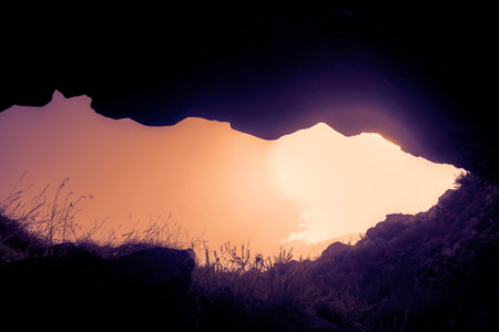 Stone hole in a cave in which there is an orange sunset skyの写真素材