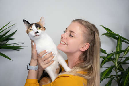 young blond woman carrying her cat trying to embrace the cat that dislikes and tries to get offの写真素材
