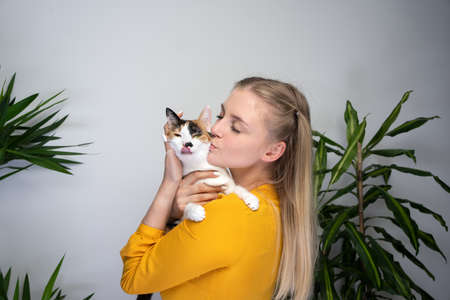 young blond woman carrying her cat kissing it on the head. the cat dislikes it and is sticking out...