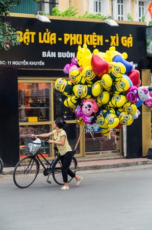 Hanoi, Vietnam - August 16, 2015: a young Vienamese helium balloon saleswoman on a bicycle, selling Despicable Me balloons in the Old Quarter.のeditorial素材