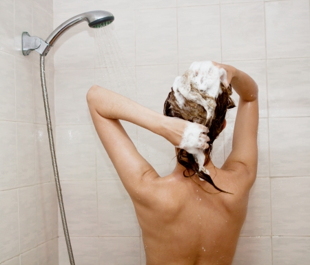 young brunette woman is taking shower and washing hairの写真素材