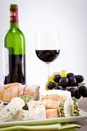 different cheese types on plate with grapes and red wine on wooden tableの写真素材