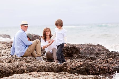 happy family sitting on rock and watching the ocean waves holiday の写真素材