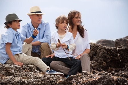 happy family sitting on rock and watching the ocean waves holiday の写真素材