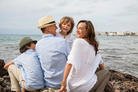 happy family sitting on rock and watching the ocean waves holiday の写真素材