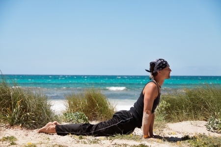 adult healthy man doing pilates yoga exercise on beach in summerの写真素材