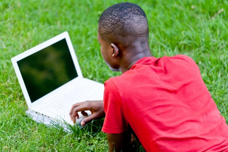 young smiling african student sitting in grass with notebook outdoor in summer manの写真素材
