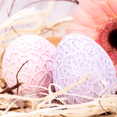 Beautiful pastel coloured Easter eggs in handcrafted intricate crocheted covers with a fresh pink Gerbera daisy in a clean straw nest for a traditional symbolic Easter celebrationの写真素材