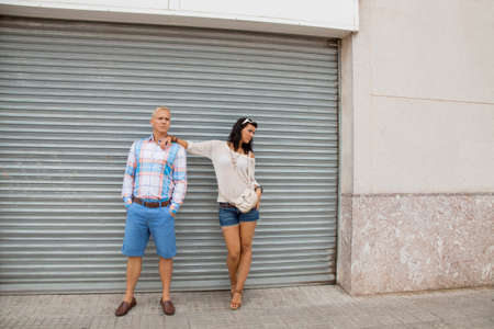 Fashionable young couple in trendy clothes posing in front of a metal door with the woman leaning on the mans shoulderの写真素材