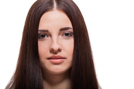 Beautiful serene young woman with a gentle expression, bare shoulders and long straight brown hair looking calmly at the camera , close up side view with turned head isolated on whiteの写真素材