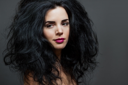 Atmospheric studio portrait of a beautiful black haired woman with a gentle serene expression gazing over her bared shoulder directly at the camera, close up head and shoulders against blackの写真素材