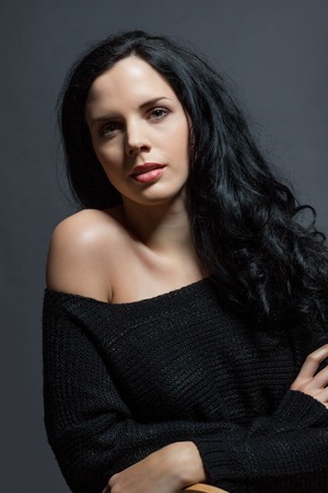 Dark moody portrait of a sultry beautiful woman with long black hair wearing a stylish off the shoulder top , head and shoulders against a grey studio backgroundの写真素材