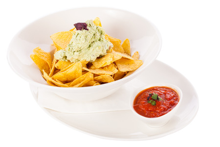 Crisp corn nachos with spicy fresh guacamole sauce and a topping of avocado served as a snack or appetizer in a white bowlの写真素材