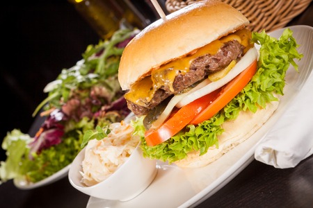 Tasty traditional cheeseburger with a ground beef patty topped with melted cheese and served with onion rings, tomato and curly leaf lettuce on a round white bread roll, close up viewの写真素材