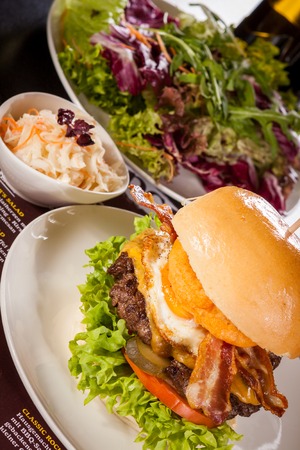 Delicious egg and bacon cheeseburger with a nutritional filling of salad ingredients, a ground beef patty, cheese, fried egg and crispy bacon on a white crusty rollの写真素材