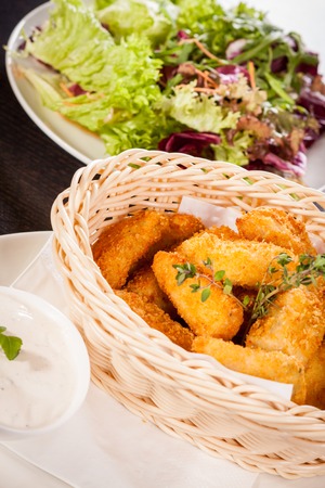 Crispy fried crumbed chicken nuggets in a wicker basket served as a finger food or appetizer with a creamy dip in a bowl alongsideの写真素材