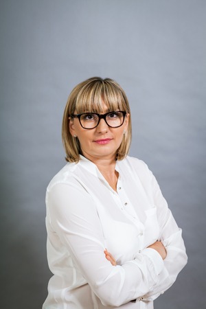 Scholarly attractive middle-aged blond woman in glasses standing looking at the camera with folded...