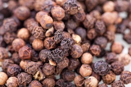 Background of whole fresh dried black peppercorns scattered on a white surface for use as a pungent...
