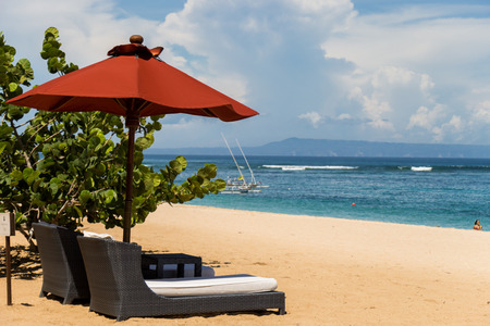 Beach umbrellas and recliners set up in the shade of tropical palm trees on a beautiful beach in Bali at a tourist resortの写真素材