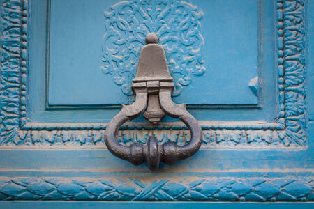 Brass door handle with a long escutcheon and lock on a colorful blue painted wooden door with a...