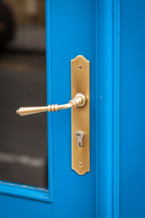 Brass door handle with a long escutcheon and lock on a colorful blue painted wooden door with a glass panel, close up viewの写真素材