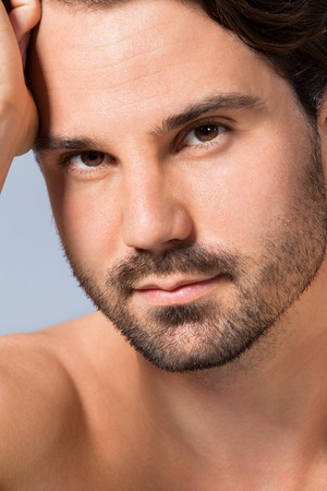 Handsome sexy bearded man posing topless looking directly into the camera with a pensive sultry expression, closeup head and shouldersの写真素材