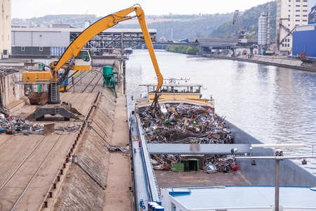 Open barge being loaded or offloaded at a wharf on an urban waterway or river by a heavy duty industrial craneの写真素材