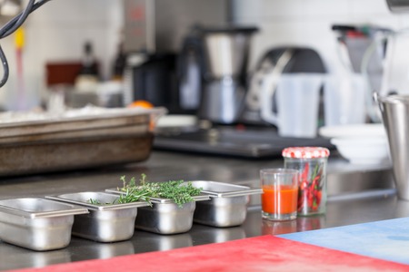 Neat interior of a commercial kitchen with wall mounted utensils and a range of different stainless steel pots arranged on a central gas hobの写真素材