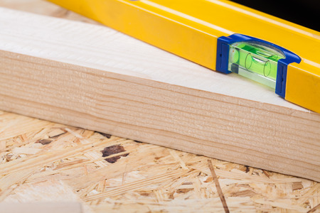 Close up view of a colorful yellow carpenters level, ruler and right angle lying on planks of new...