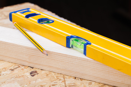 Close up view of a colorful yellow carpenters level, ruler and right angle lying on planks of new hardwood together with a pencil for measurements in a carpentry, construction, DIY and joinery conceptの写真素材