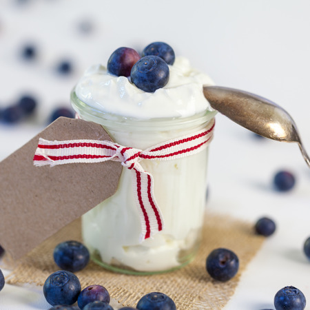 Jar of clotted cream or yogurt with fresh blueberries tied with a decorative ribbon and blank gift tag with copyspace for your text served on a square of hessian for healthy country cuisineの写真素材
