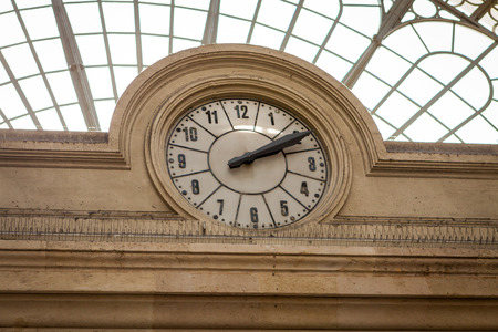 Circular clock inset into a stone building facade under a domed glass roof at a mall, station or terminal viewable by the public on their travelsの写真素材