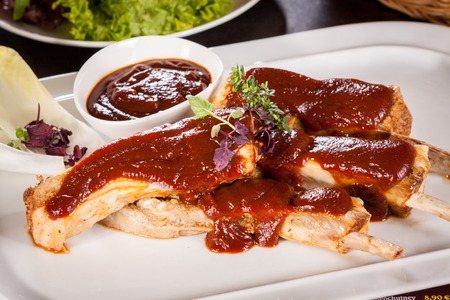 Delicious grilled pork ribs served with a rich brown gravy or BBQ sauce garnished with fresh herbs , close up side viewの写真素材
