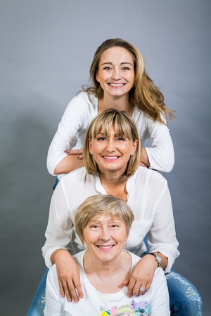 Three generations of attractive women with blond hair and a striking family resemblance posing together arm in arm looking at the camera with friendly smilesの写真素材