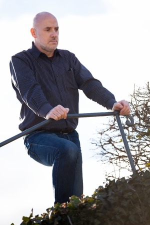 View from below of a thoughtful middle-aged man sitting on a flight of steps staring into the distance with a serious expression against a blue skyの写真素材