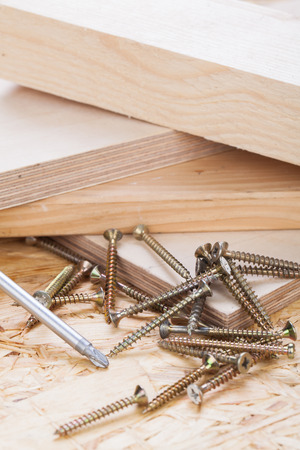 Close up view of a head screwdriver and threaded metal wood screws with one screw inserted into a plank of wood in a carpentry, joinery, and construction conceptの写真素材