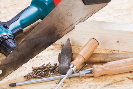 Battery-operated portable hand drill with timber, screwdrivers and screws surrounded by fresh wood...