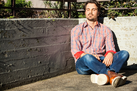 Man sitting on the ground with feet crossed under the sunの写真素材