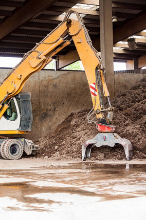 Heavy duty excavator doing earth moving parked undercover in an open warehouse in front of a huge...