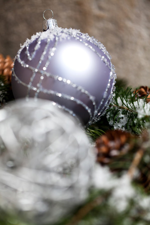 Silver glitter textured Christmas bauble on the branch of a pine or fir tree sprinkled with snow and cones with handcrafted straw decorations in the backgroundの写真素材