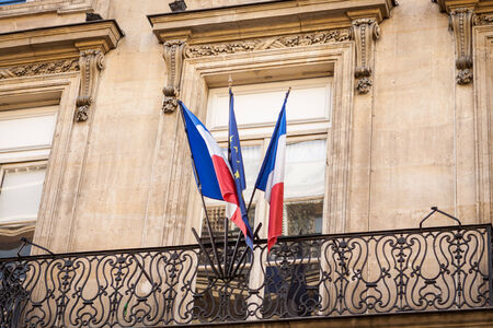 Flag of France fluttering on a pole placed on the top of a vintage building, under a serene blue sky with white cloudsの写真素材